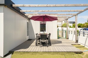 En täckt uteplats med ett bord och stolar, en pergola ovanför och utsikt över det omgivande området.