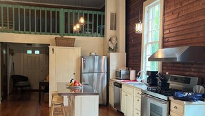 A kitchen with wooden floors, a central island, stainless steel appliances, and a view of the outdoors through a window. - Charming 2-bedroom cottage w WiFi, AC in tranquil Syria w deck sounds Rose River (Syria)