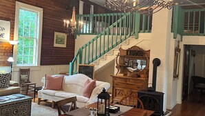 A cozy room with a staircase, a fireplace, a sofa, and a dining table. - Charming 2-bedroom cottage w WiFi, AC in tranquil Syria w deck sounds Rose River (Syria)