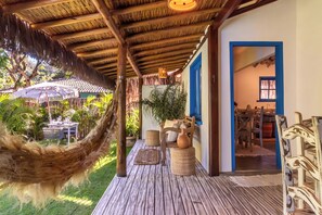 A wooden deck with a hammock, wicker furniture, and a view of a garden. - Awe Villa Boutique e Beach Club (Porto Seguro)