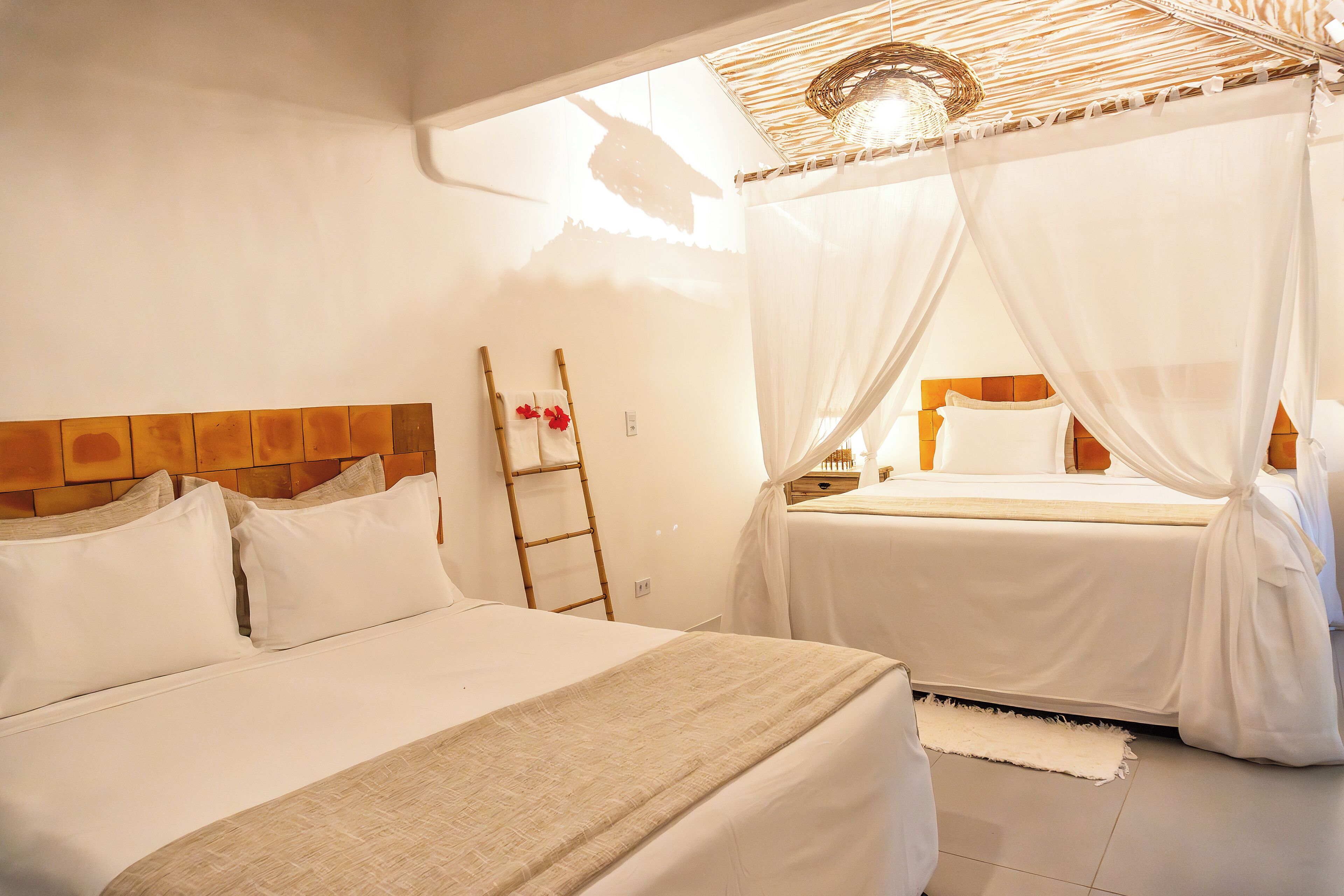 A hotel room with two beds, a wooden headboard, a ladder, and a woven ceiling light fixture.