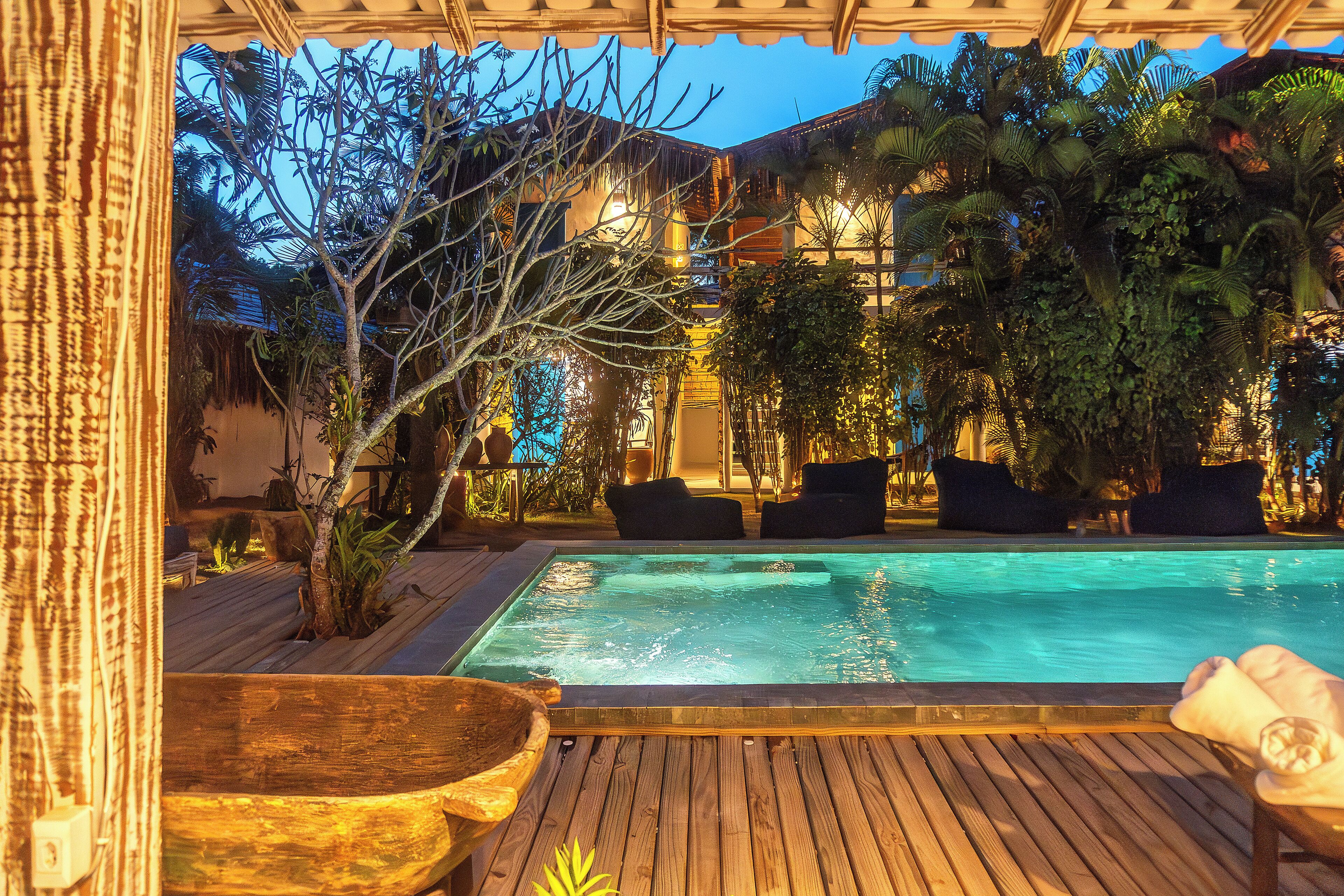 Una terraza de madera con piscina, sillas de descanso y plantas tropicales.