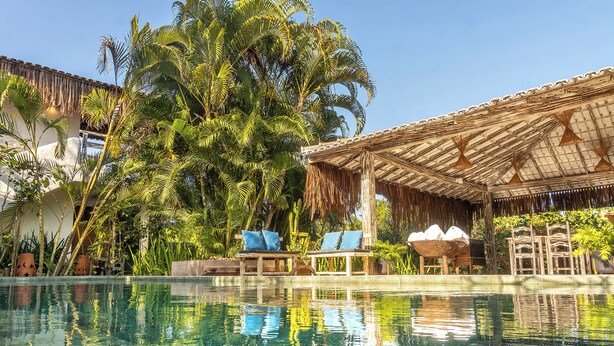 A pool area with lounge chairs and a thatched-roof structure. - Awe Villa Boutique e Beach Club (Porto Seguro)