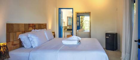 Una habitación de hotel con cama, mesita de noche con lámpara, espejo y maleta.