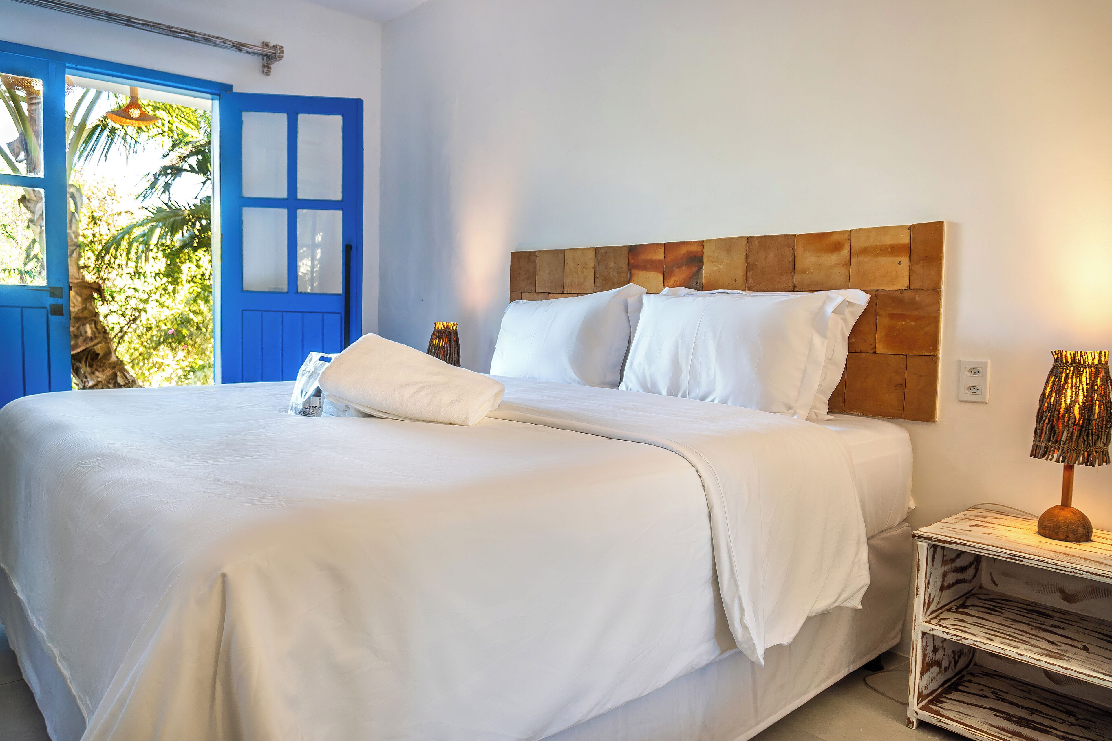 Una cama bien tendida con sábanas blancas, cabecera de madera y lámpara de noche.