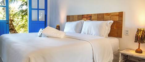 Una cama bien tendida con sábanas blancas, cabecera de madera y lámpara de noche.