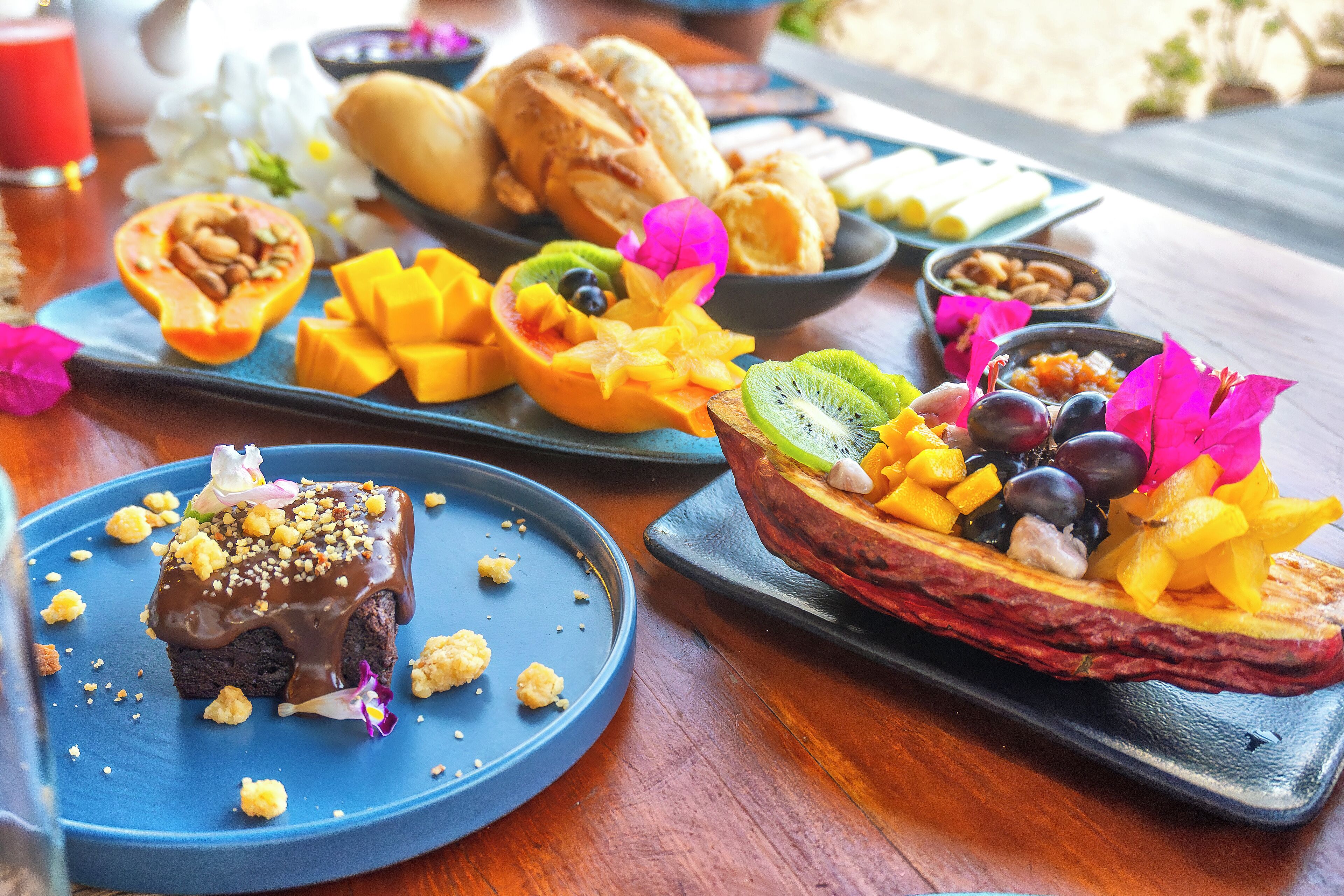 A variety of breakfast items on a wooden table, including pastries, fruits, and a chocolate dessert.