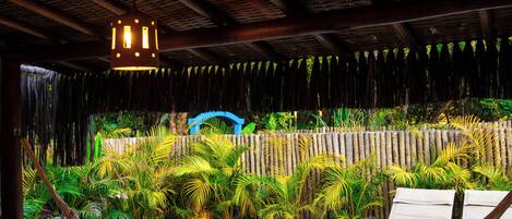 Un'amaca sopra un pontile in legno con piscina, circondata da vegetazione lussureggiante e una recinzione in legno.