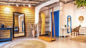 A room with a rustic brick wall, a wooden swing, a mirror, a blue door, and a small table with a vase. - Awe Villa Boutique e Beach Club (Porto Seguro)