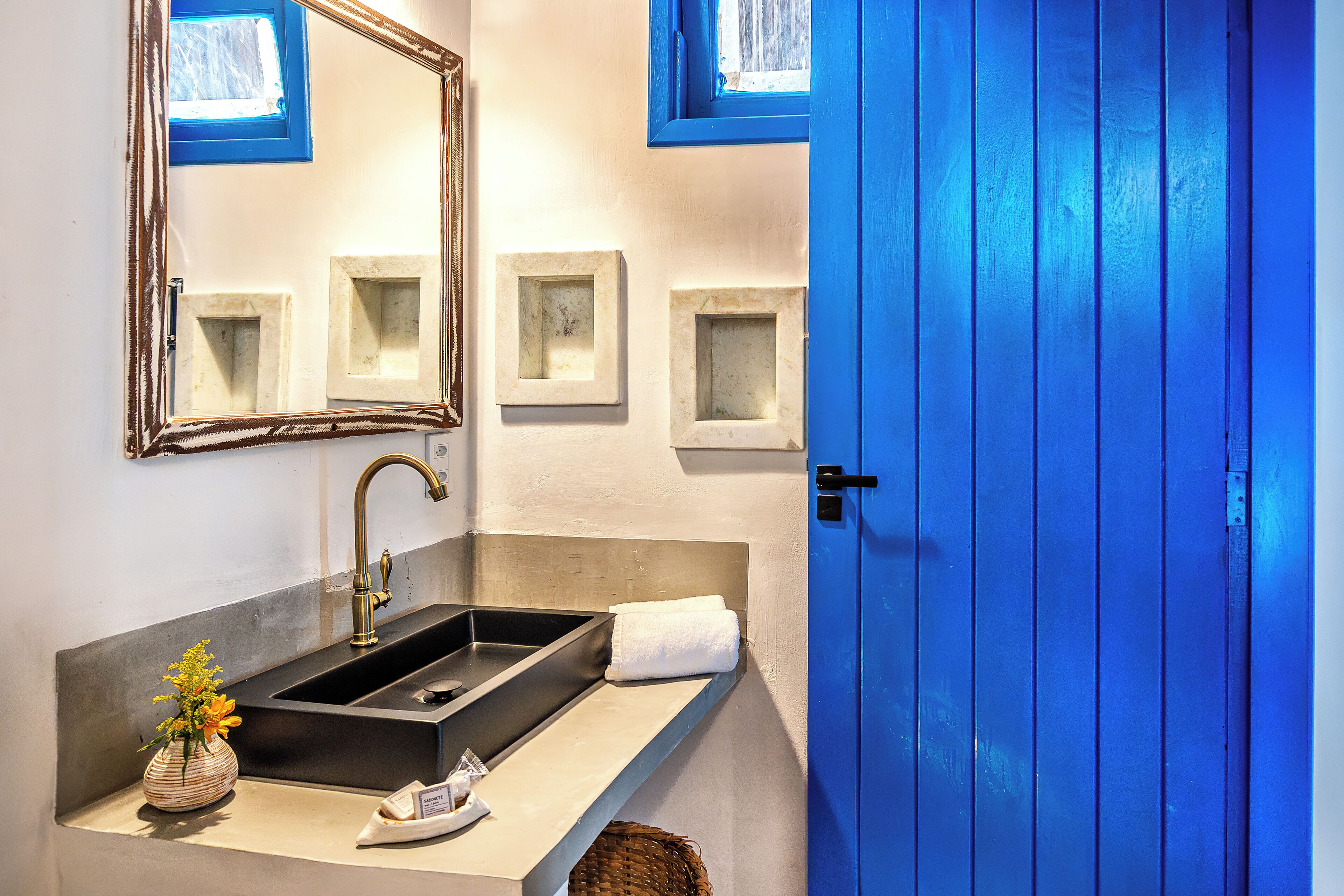 A bathroom with a black sink, a mirror, a towel, and a small vase with flowers.