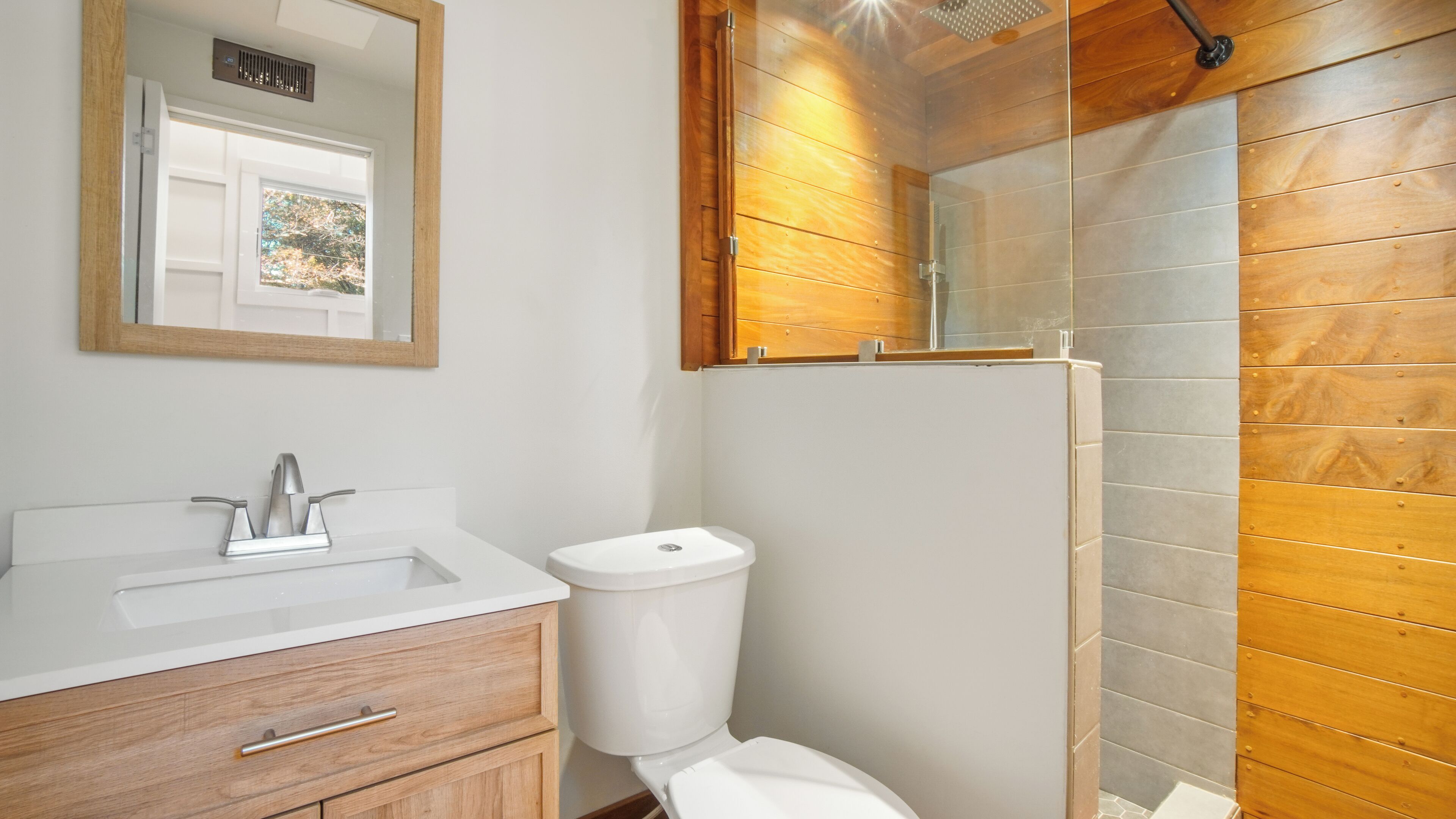 A bathroom with a white sink, wooden vanity, a toilet, and a glass shower enclosure with wooden paneling.