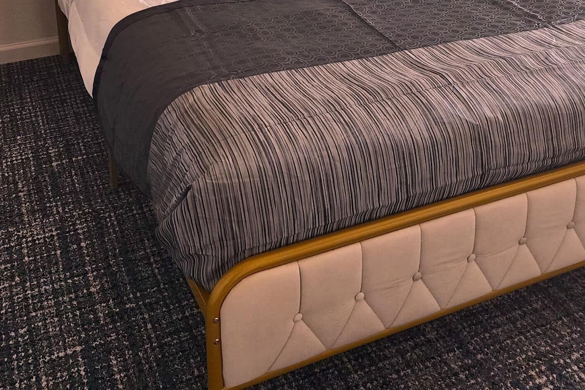 Cama bem arrumada com manta listrada e cabeceira estofada.