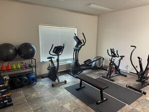 A home gym with exercise equipment, a bench, and a rack of dumbbells. - The Enchanted Suites & Residence  (Roswell)