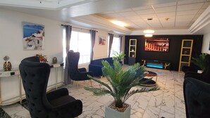 A spacious lobby with marble flooring, black upholstered chairs, a potted plant, and a television screen. - The Enchanted Suites & Residence  (Roswell)