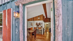 Un intérieur rustique en bois, avec un espace repas et une cuisine visibles à travers une porte ouverte.