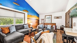 A modern living room with a large window, a sofa set, a coffee table, and a TV.