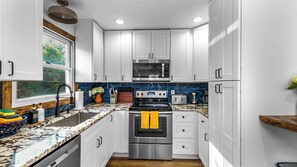 A modern kitchen with white cabinets, a stainless steel oven, a microwave, and a granite countertop.