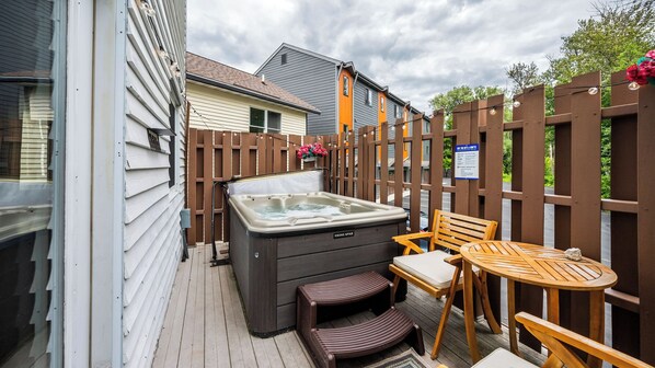 A hot tub with a wooden deck, a table, and chairs.