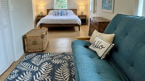 Ein Schlafzimmer mit einem Bett, einem blauen Sofa, einer Korbschachtel und einem gemusterten Teppich.