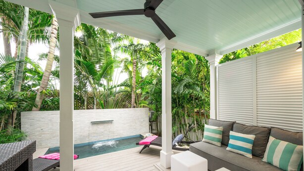 A covered outdoor area with a pool, seating, and lush greenery.