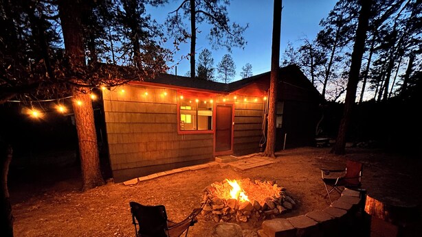 Una cabaña con una fogata, asientos exteriores y luces colgantes.