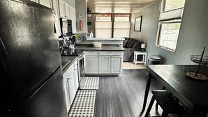 Una cocina equipada con refrigerador, estufa y lavamanos. Se aprecia una ventana con vistas a árboles y una puerta que da a otra habitación.