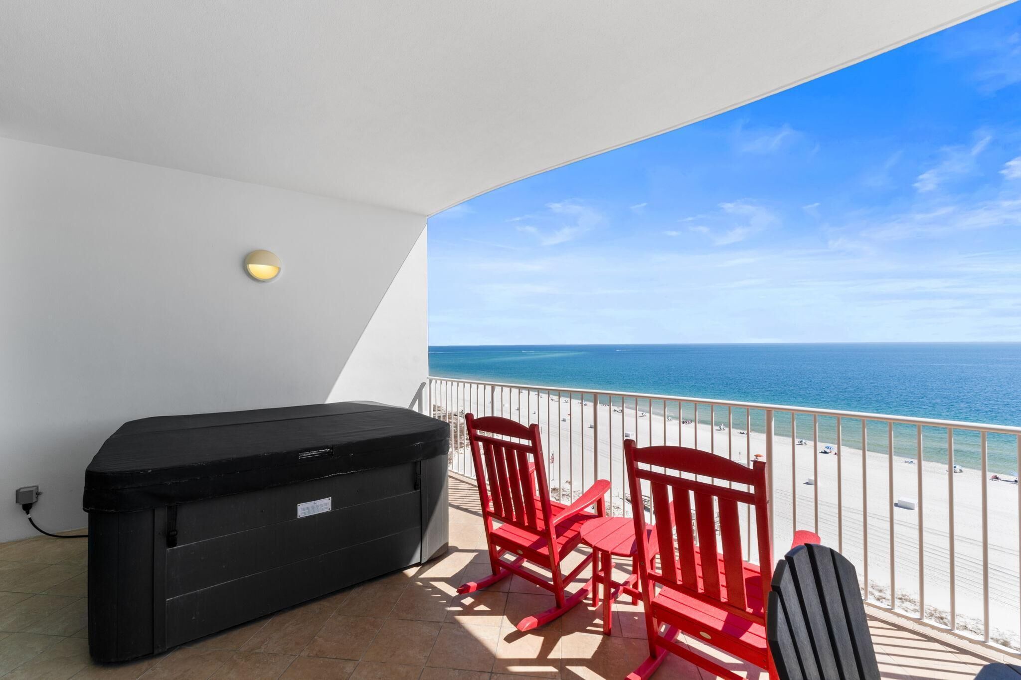 A balcony with a grill, two red chairs, and a view of the beach and ocean.