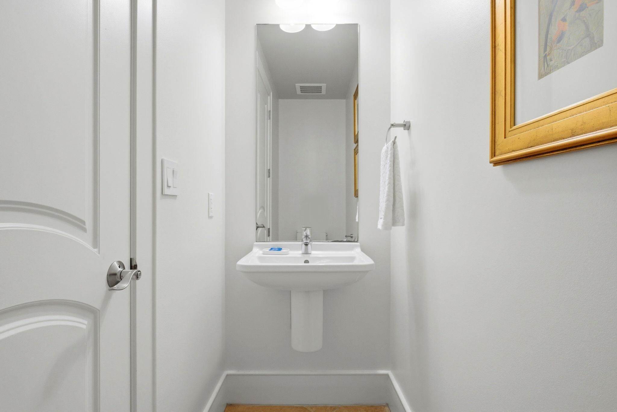A narrow bathroom with a white sink, a mirror, and a towel hanging on the wall.