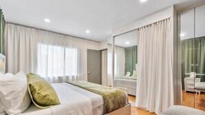 A modern bedroom with a large bed, a bedside table, a mirror, and a view of a bathroom. - Modern Lush Green Escape (Fort Lauderdale)