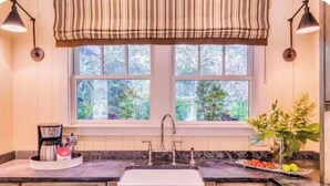 Eine Küche mit Fenster, Spüle, Kaffeemaschine und Blumen in einer Vase.