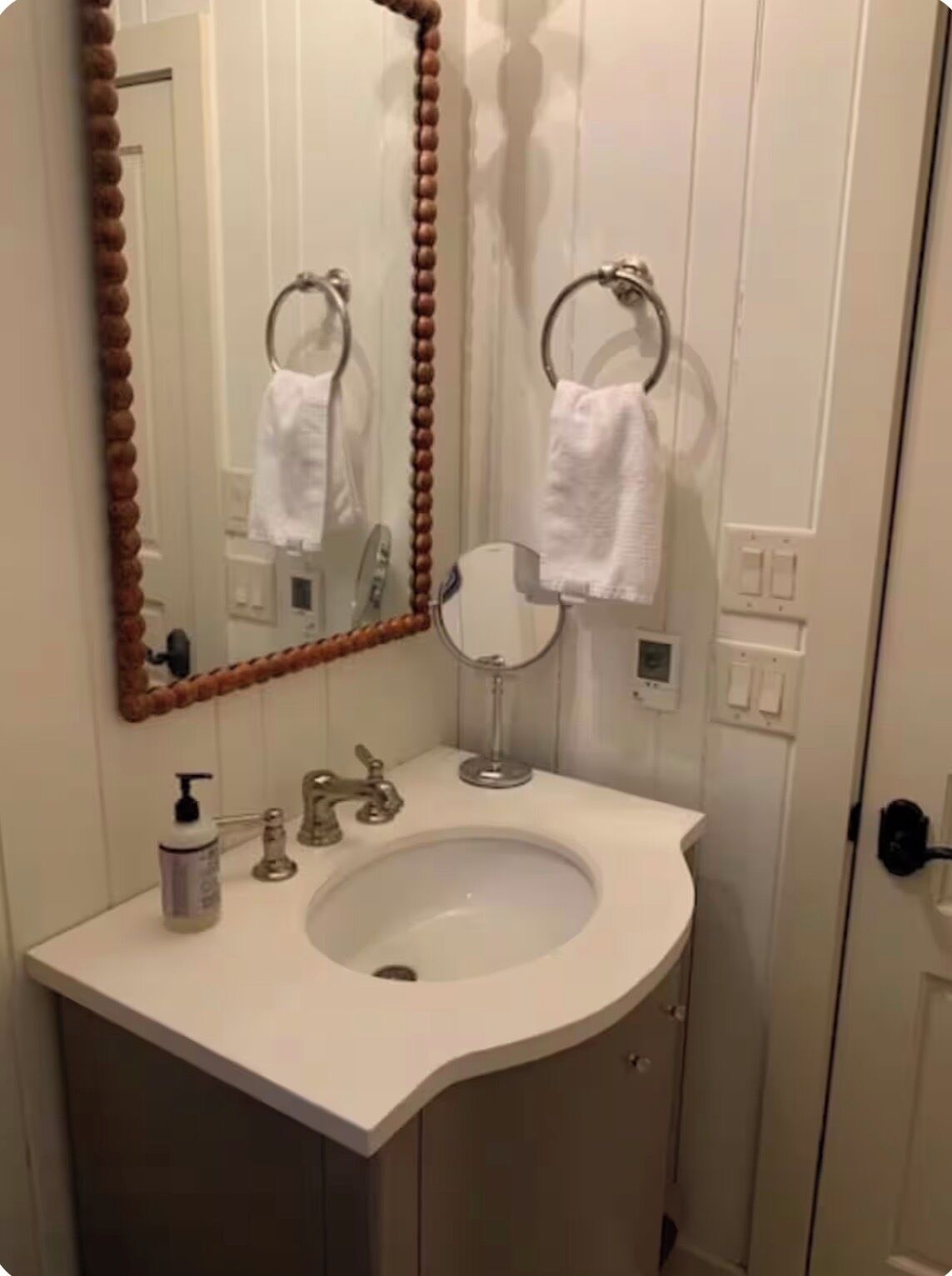 A bathroom with a white sink, a mirror with a wooden frame, a towel rack, and a soap dispenser.
