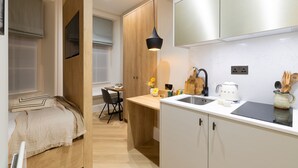 A compact kitchen with a wooden dining area, a white countertop, and a hanging light fixture. - Cozy Suite in Sloane Square (London)