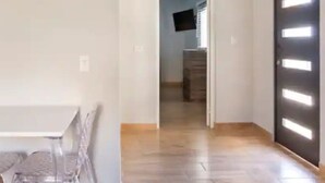 Een kamer met een witte tafel en stoelen, een houten vloer en een deur met verlichte panelen.
