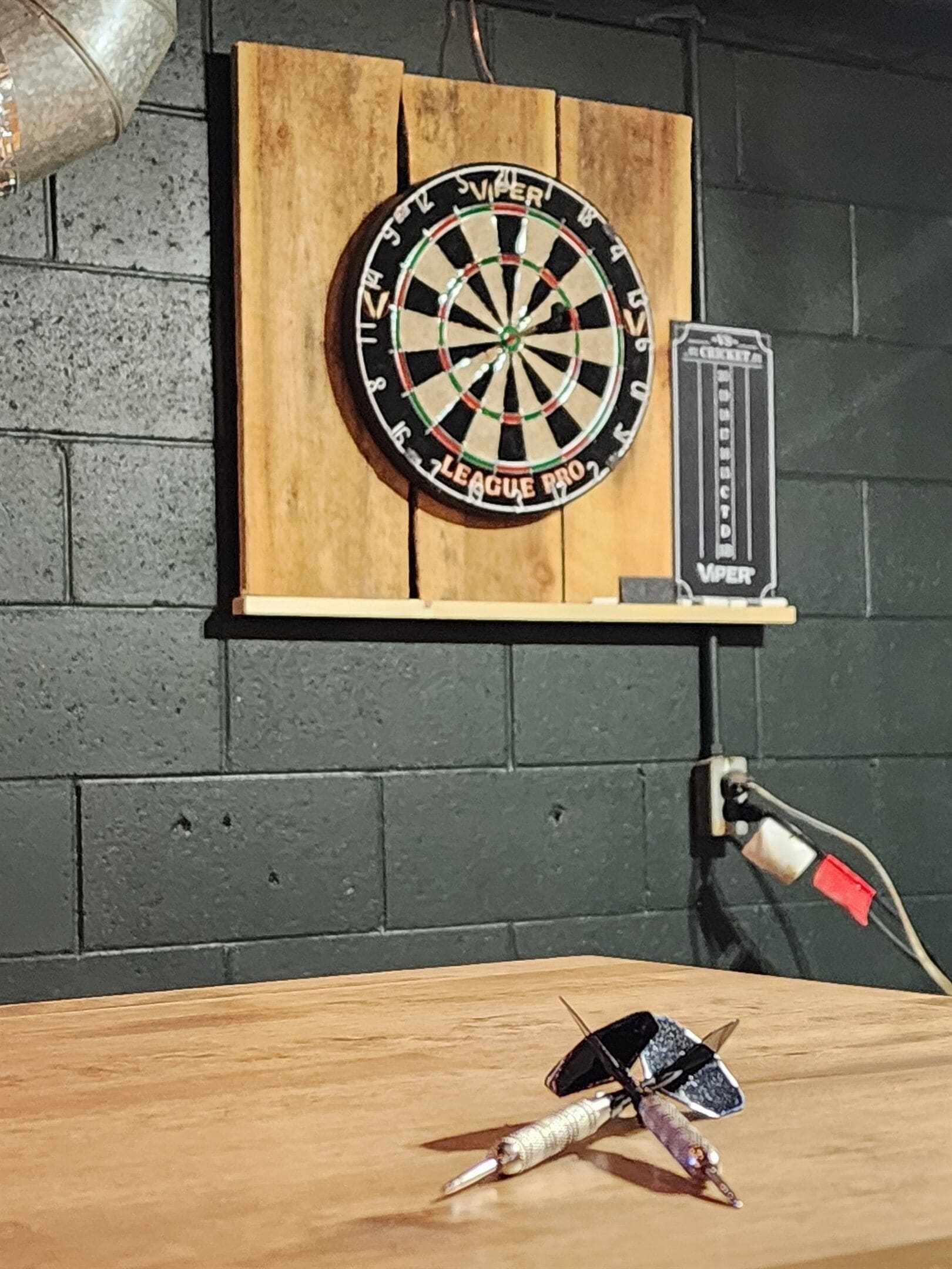 Une cible de fléchettes fixée sur un panneau de bois, avec une autre cible de fléchettes et une fléchette posées sur une table en dessous.