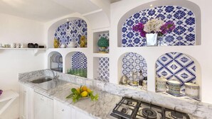 Una cocina con armarios blancos, encimera de mármol y azulejos azules y blancos en las paredes.