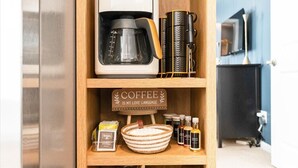 A coffee maker on a shelf with a sign that says "COFFEE IS MY LOVE LANGUAGE." Below are coffee beans, a coffee grinder, and a coffee pot.