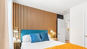A hotel room with a bed, a wooden slat wall, a blue headboard, and two bedside lamps.