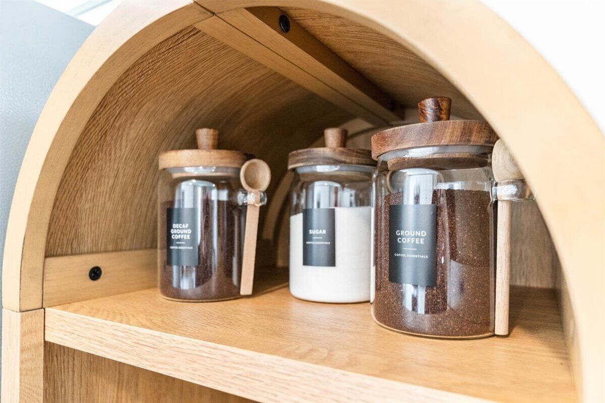 A wooden cabinet with three glass jars labeled 'Decaf Ground Coffee,' 'Sugar,' and 'Ground Coffee.'
