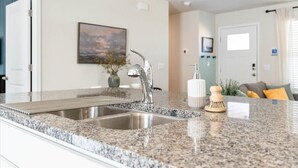 A kitchen with granite countertops, stainless steel sink, and a painting on the wall.