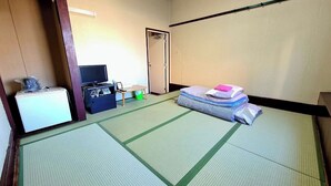 A room with tatami mats, a bed with pillows, a television, a small table, and a cabinet. - Nishiki Guest House (Kadoma)