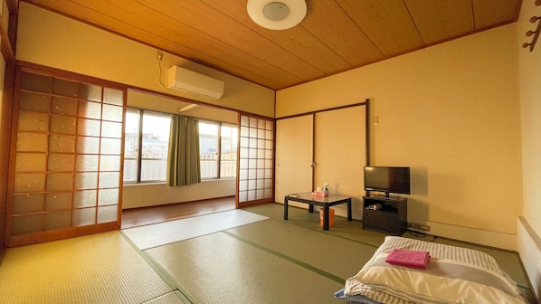 A traditional Japanese room with tatami flooring, a sliding door, a television, and a small table with a bottle. - Nishiki Guest House (Kadoma)