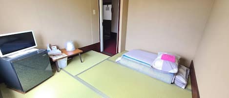 A hotel room with a bed, a desk with a computer, a chair, a small table, and a door leading to another room.