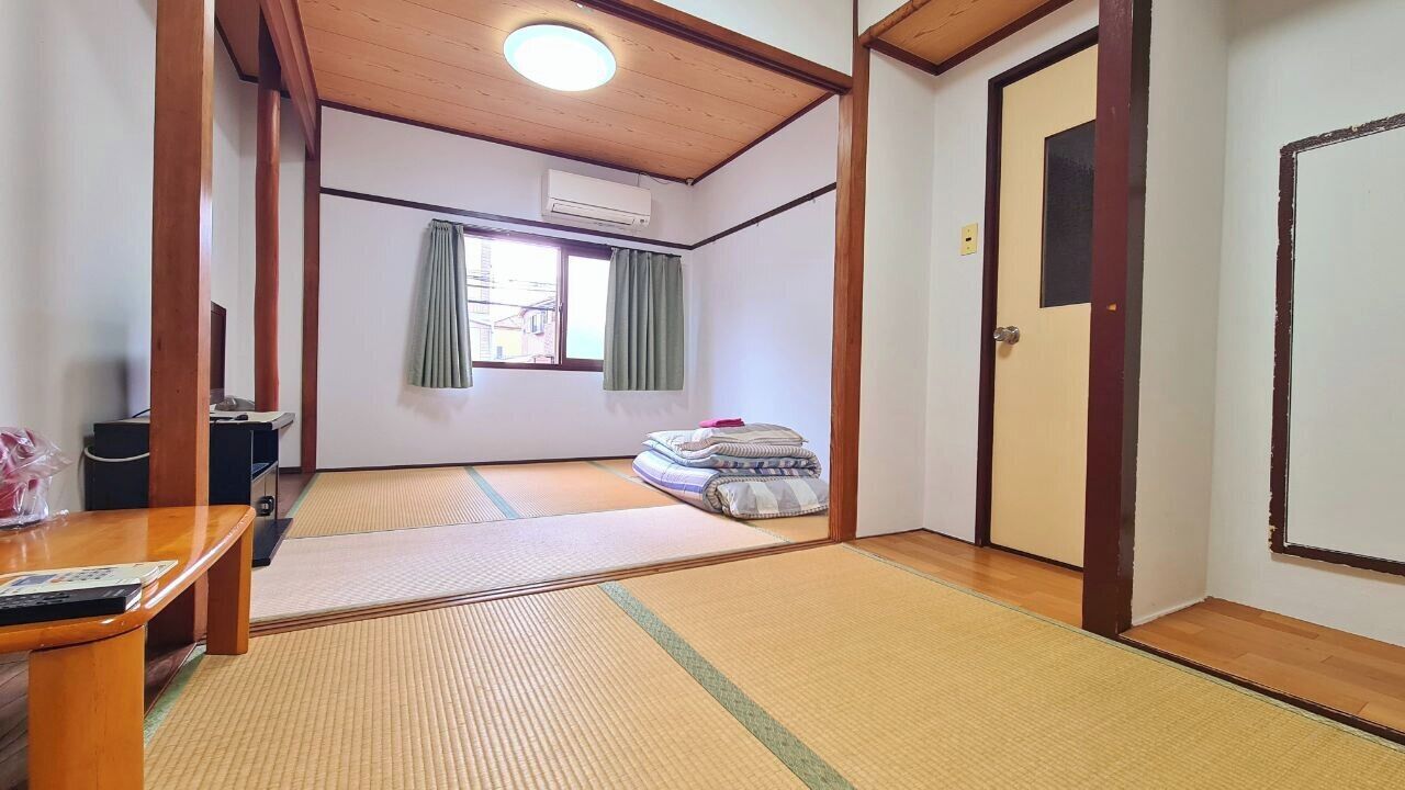 A traditional Japanese room with tatami flooring, a wooden ceiling, a window with curtains, and a door.