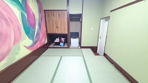 A room with tatami flooring, a wardrobe, a television, and a small table with items on it. - Nishiki Guest House (Kadoma)