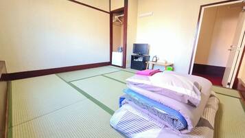 A traditional Japanese room with tatami flooring, a bed with pillows, a television, and a small desk with a chair.