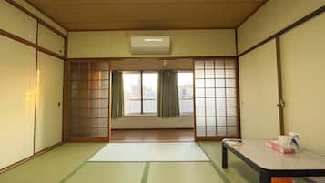A traditional Japanese room with tatami flooring, sliding doors, a small table, and a window with curtains.