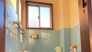 Ein Badezimmer mit Toilette, einem Fenster und einem Paar Hausschuhen auf dem Boden.