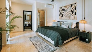 A bedroom with a bed, a ceiling fan, a wall-mounted light fixture, and a patterned rug. - Ocean Elegance
Contemporary Beachfront Escape at El Faro Resort Living (Playa del Carmen)