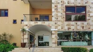A hotel entrance with a stone facade, a balcony, and a staircase leading to the entrance. - Ocean Elegance
Contemporary Beachfront Escape at El Faro Resort Living (Playa del Carmen)
