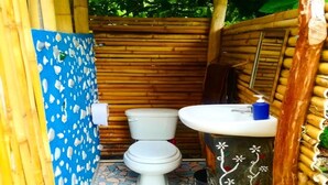 Een kleine, afgesloten badkamer met toilet en wastafel, bamboe wanden en een betegelde vloer.